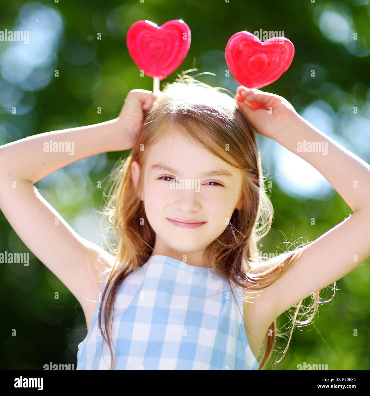 Cute little girl eating huge heartshaped lollipops outdoors on