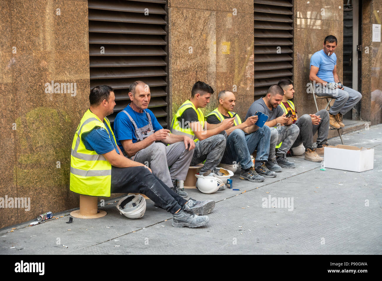 Seven workmen having a break, smlking, checking phones, chatting and relaxing, Middlesex Road, Spitalfields, east London, England, UK Stock Photo