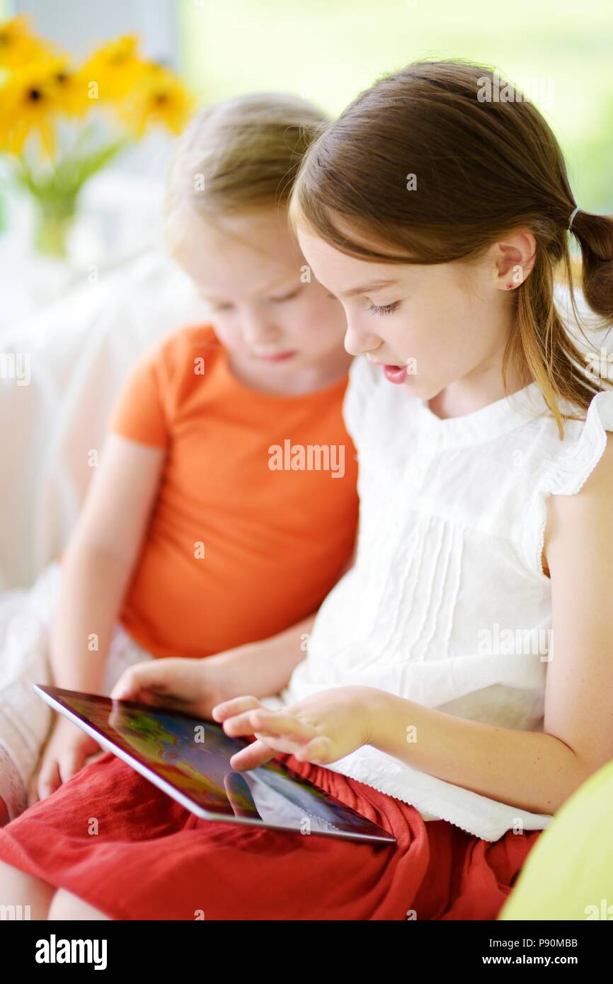Two adorable little sisters playing with a digital tablet at home Stock ...