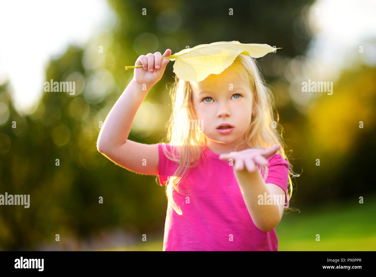 Cute little girl holding big yellow leaf above her head, playing as if it was raining Stock Photo