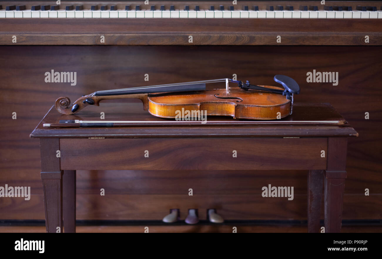 Vintage Violin and Bow Laying on Bench with Piano in Background Stock Photo