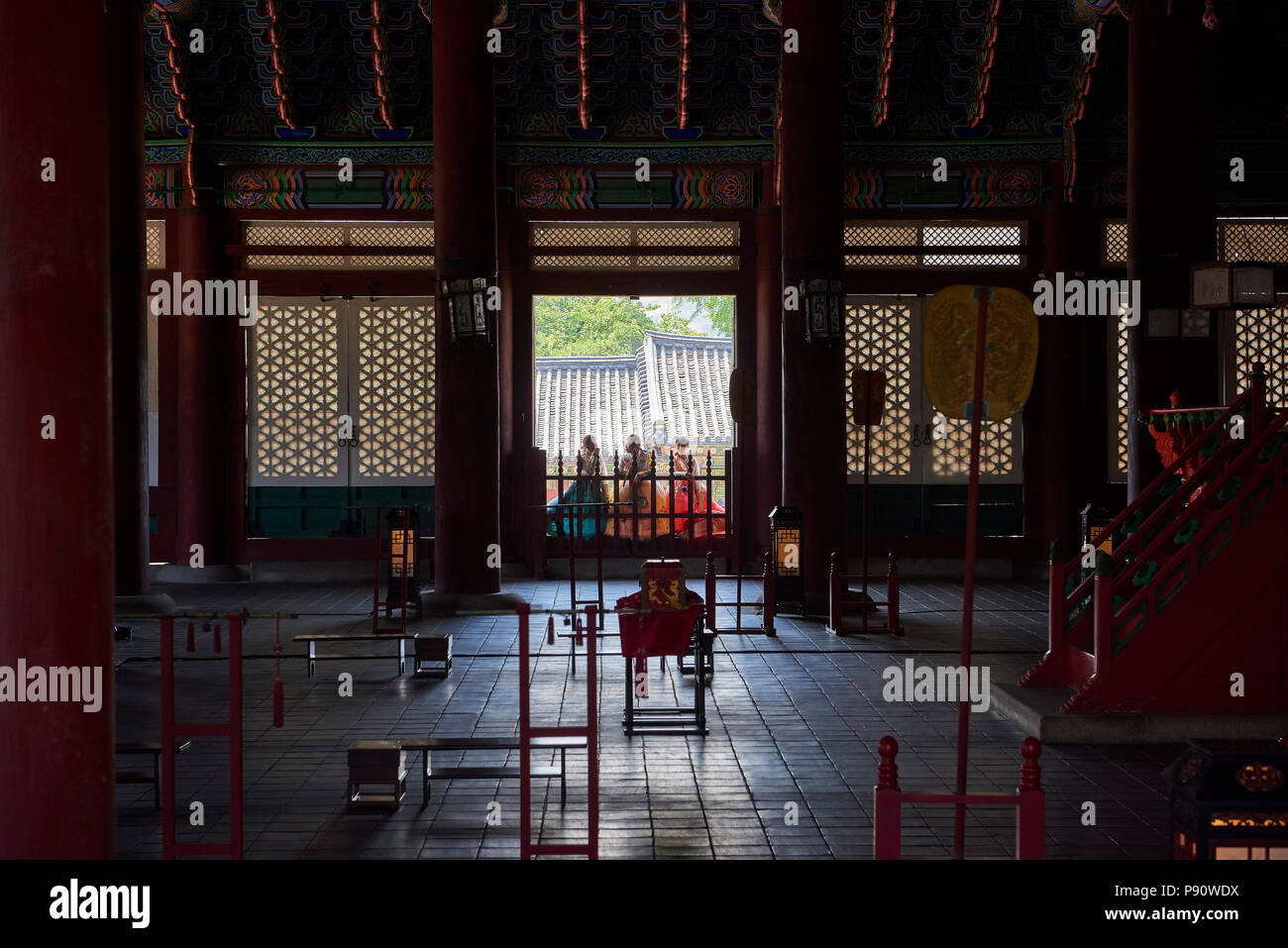 Three girls dressed in traditional Korean dresses are silhouetted at a window in the Throne Hall in Gyeongbokgung Palace, Seoul, South Korea. Stock Photo