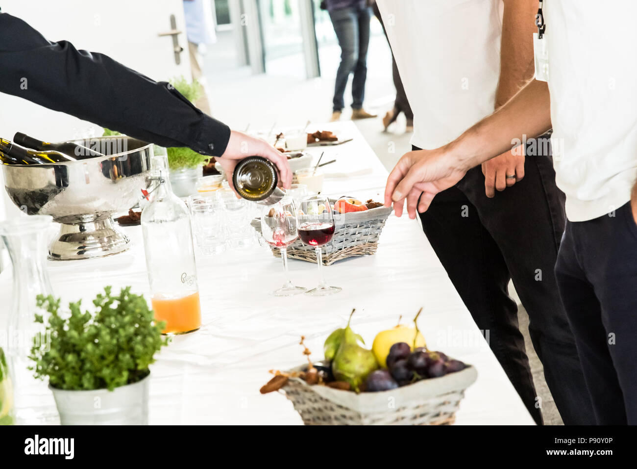 Waiter Pouring Red Wine Glass to Two Men on White Buffet Table Stock Photo
