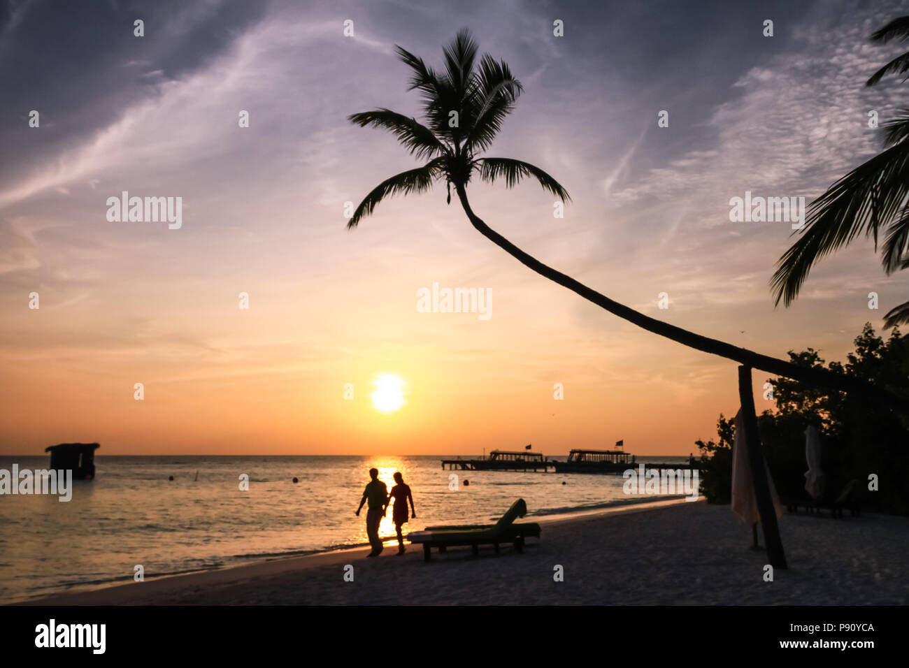 Couple Walking on Maldivian Island Resort Beach at Sunset Stock Photo