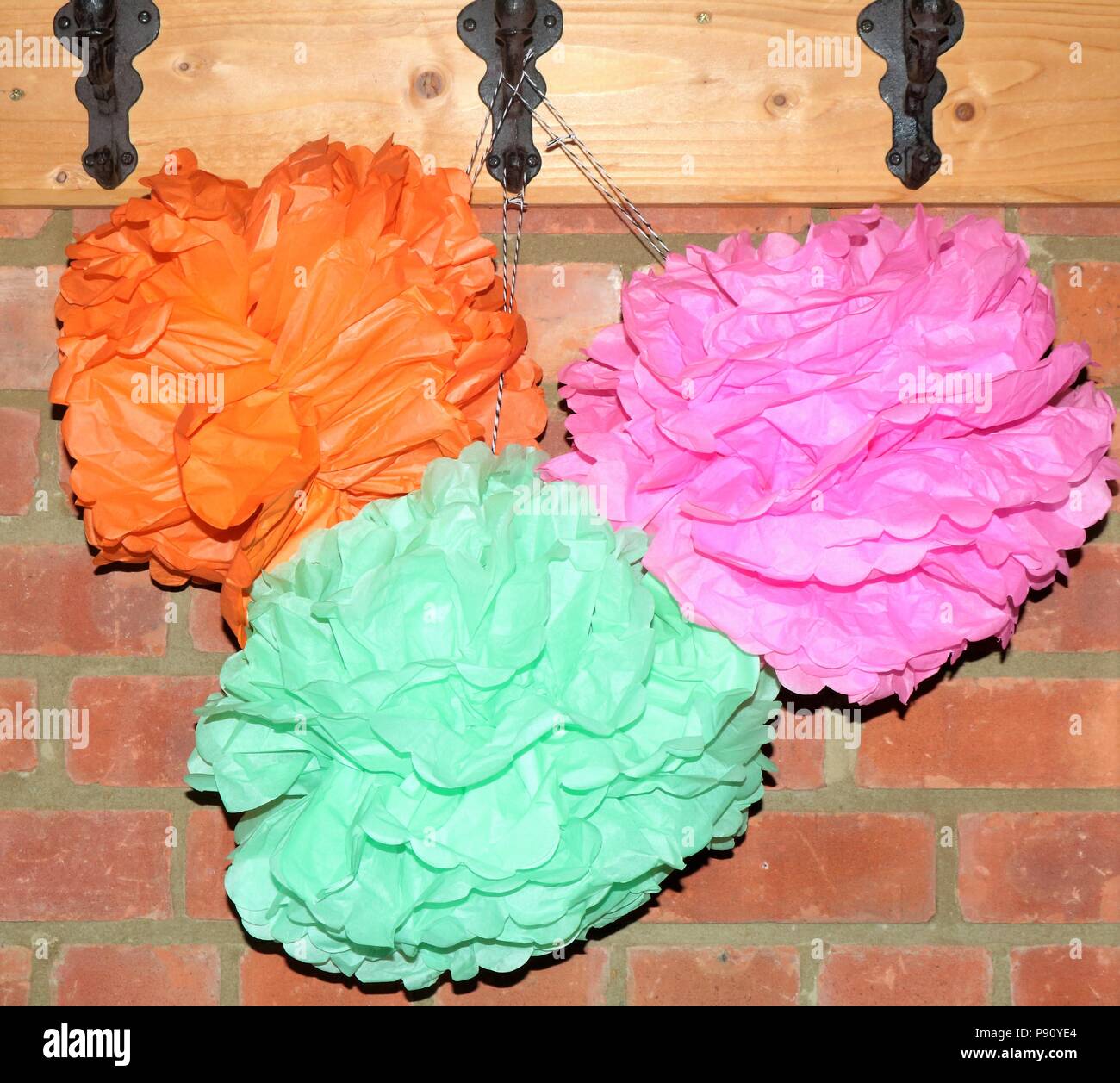 Colourful paper pom poms hanging on hooks against a brick wall. Stock Photo