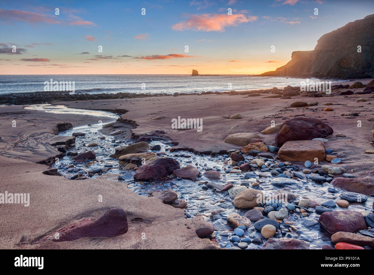 The beach at Saltwick Bay, North Yorkshire, England, UK, at sunrise. The sea stack is known as Black Nab. Stock Photo