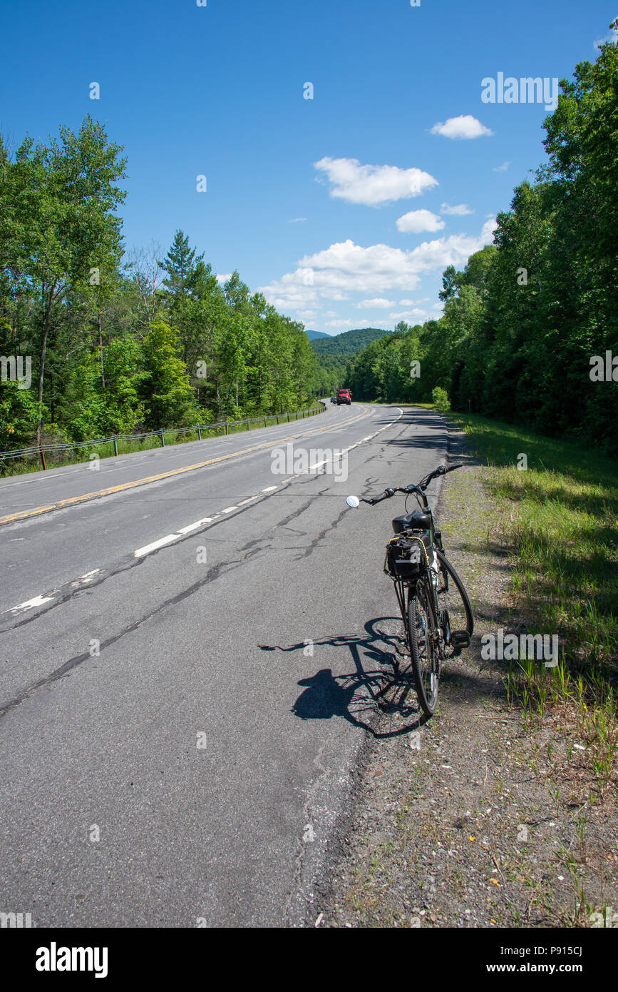 A bicycle on the side of a highway in the Adirondack Mountains, NY USA on a bright sunny day with white clouds and a deep blue sky. Stock Photo