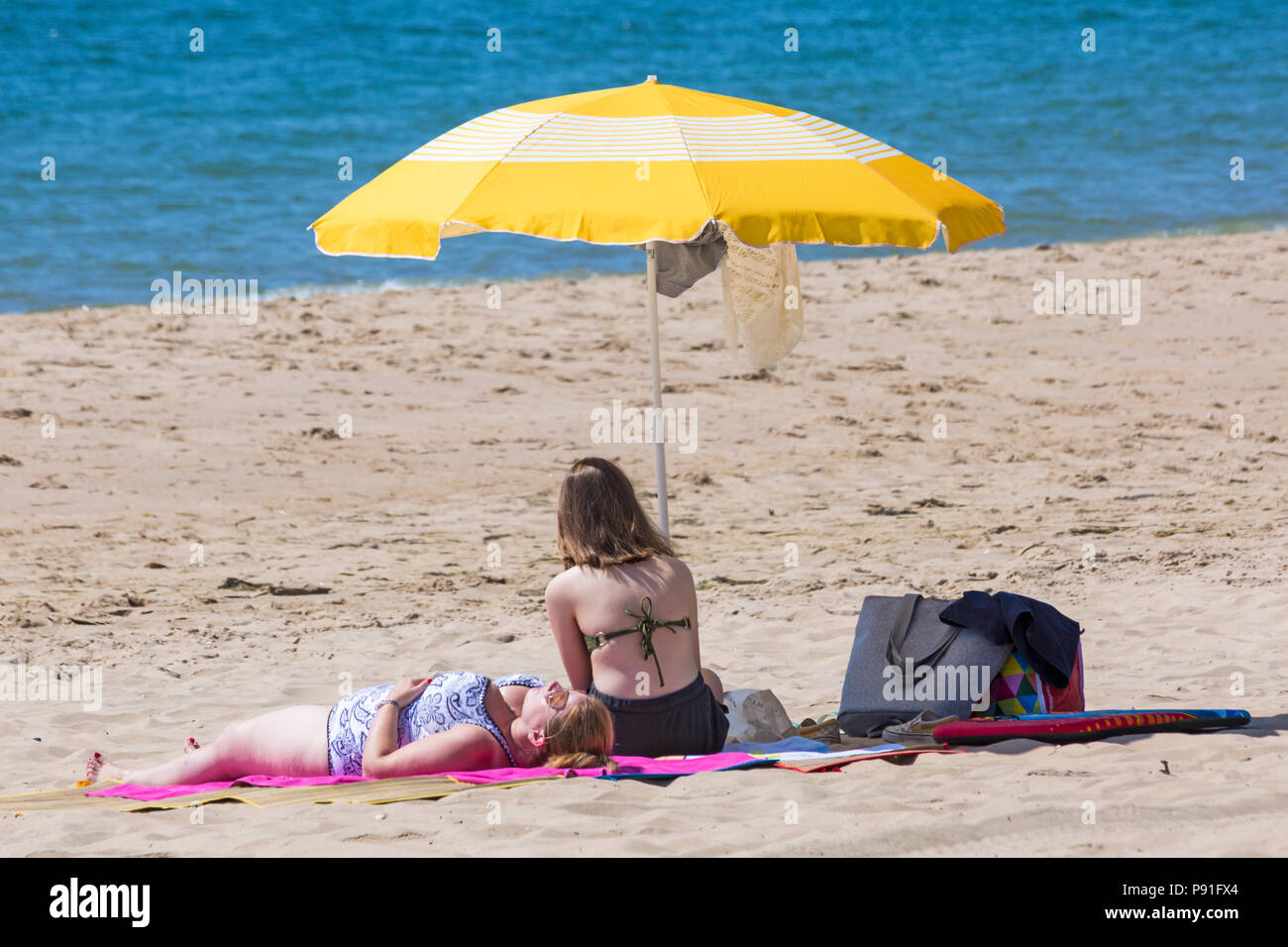 Bournemouth, Dorset, UK. 14th July 2018. UK weather: The heatwave continues with another hot sunny day, as sunseekers make the most of the glorious weather and head to the seaside at Bournemouth beaches. Women sunbathing on beach with yellow parasol. Credit: Carolyn Jenkins/Alamy Live News Stock Photo
