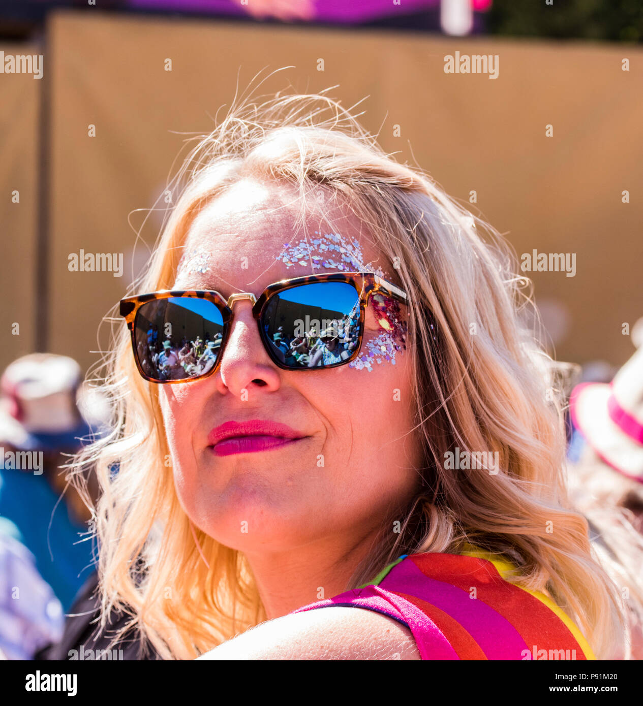 portrait of female festival goer, wearing sunglasses, with fellow festival goers reflected in sunglasses, at Latitude Festival, Henham Park, Suffolk, England, 14th July, 2018 Stock Photo