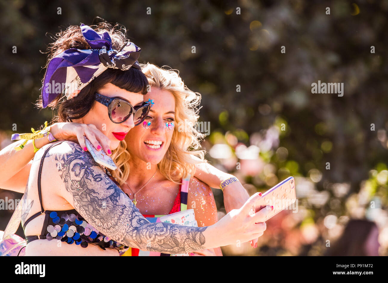 Two female festival goers in colourful dresses, taking a selfie, using smartphone, at Latitude Festival, Henham Park, Suffolk, England, 14th July 2018 Stock Photo