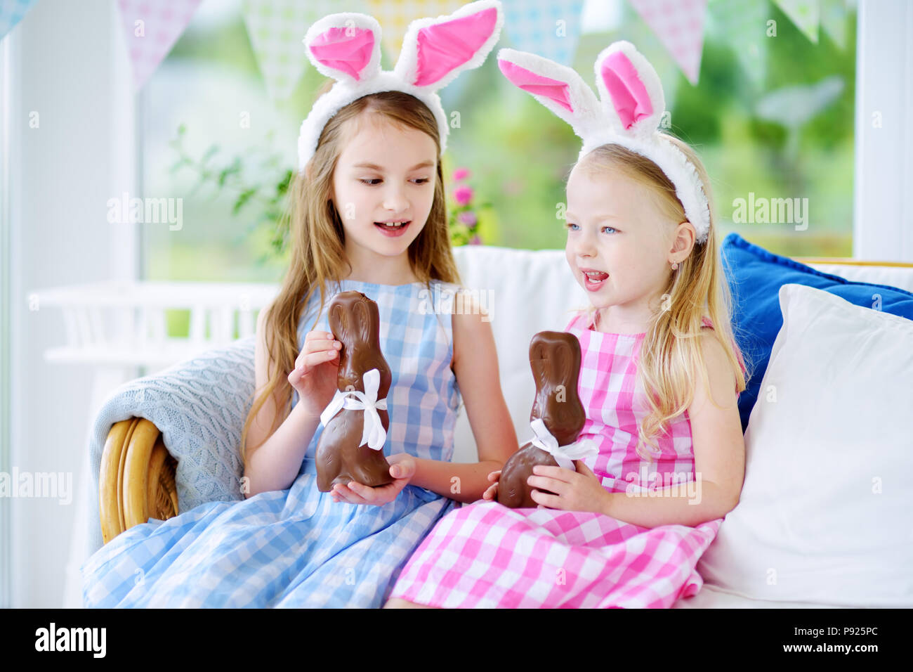 Two cute little sisters wearing bunny ears eating chocolate Easter