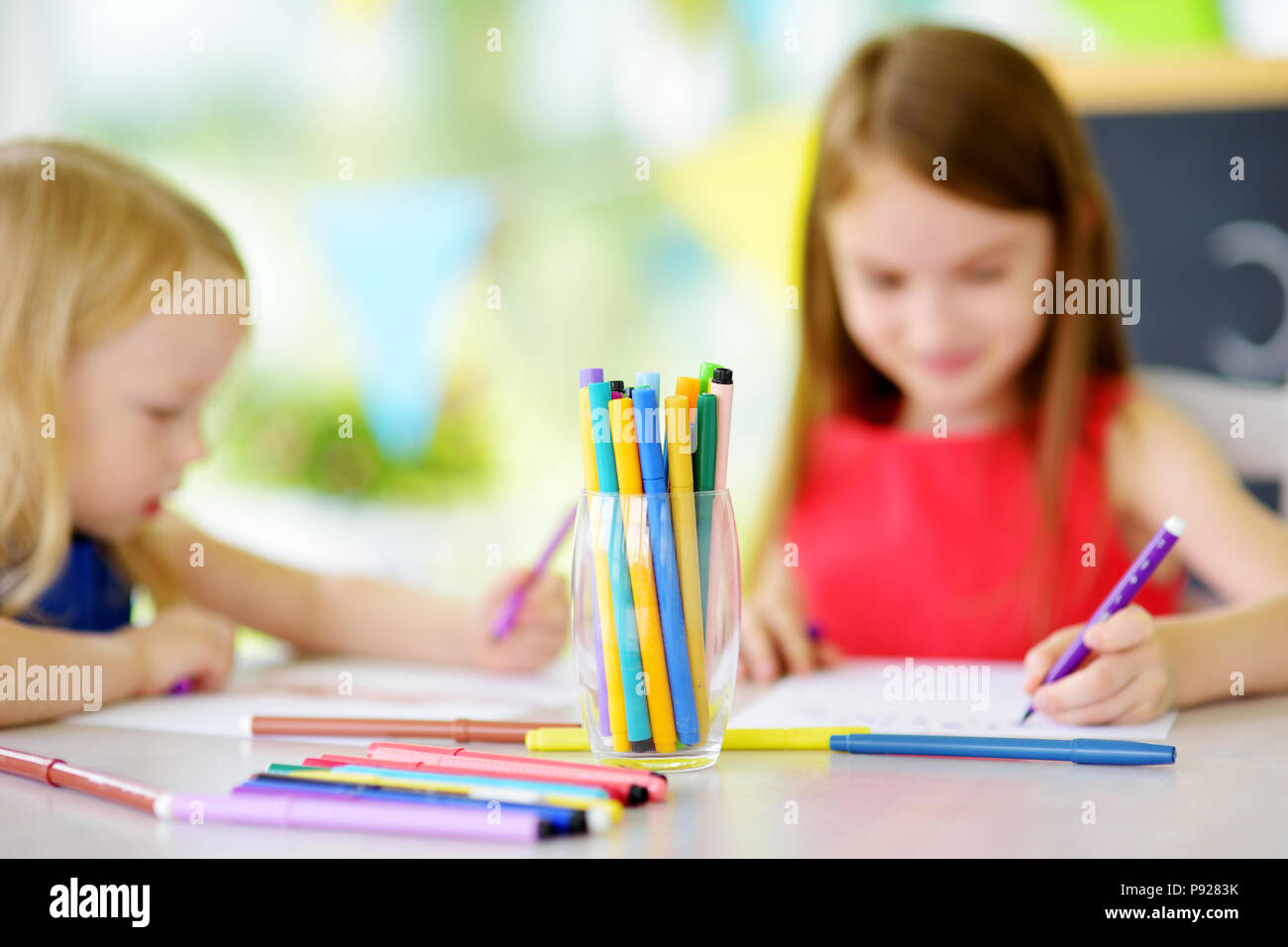 Two cute little sisters drawing with colorful pencils at a daycare ...