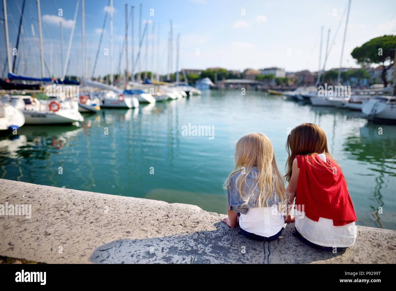 Two cute little sisters watching small yachts in harbor in Desenzano del Garda on beautiful autumn day, Lombardy, Italy Stock Photo
