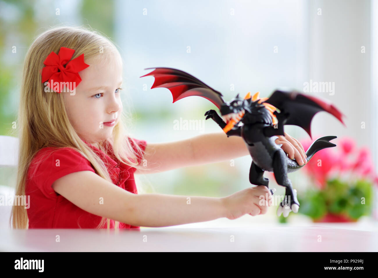 Cute little girl playing with toy dragon at home Stock Photo