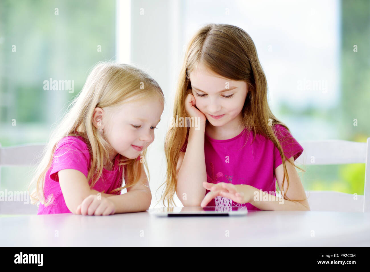 Two adorable little sisters playing with a digital tablet at home ...