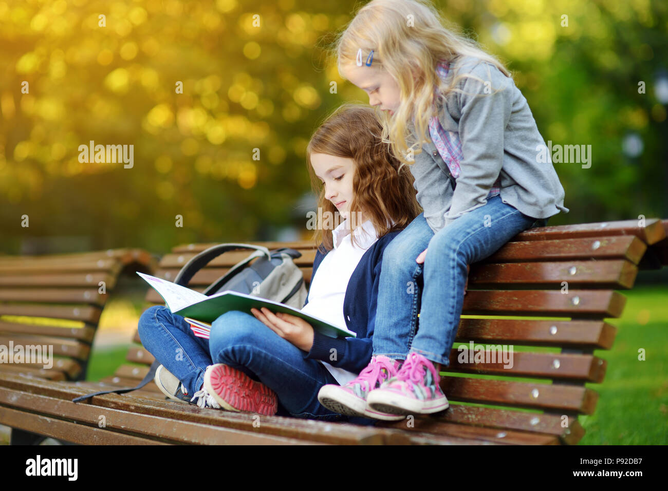 Adorable little schoolgirls studying outdoors on bright autumn day. Young students doing their homework. Education for small kids. Back to school conc Stock Photo