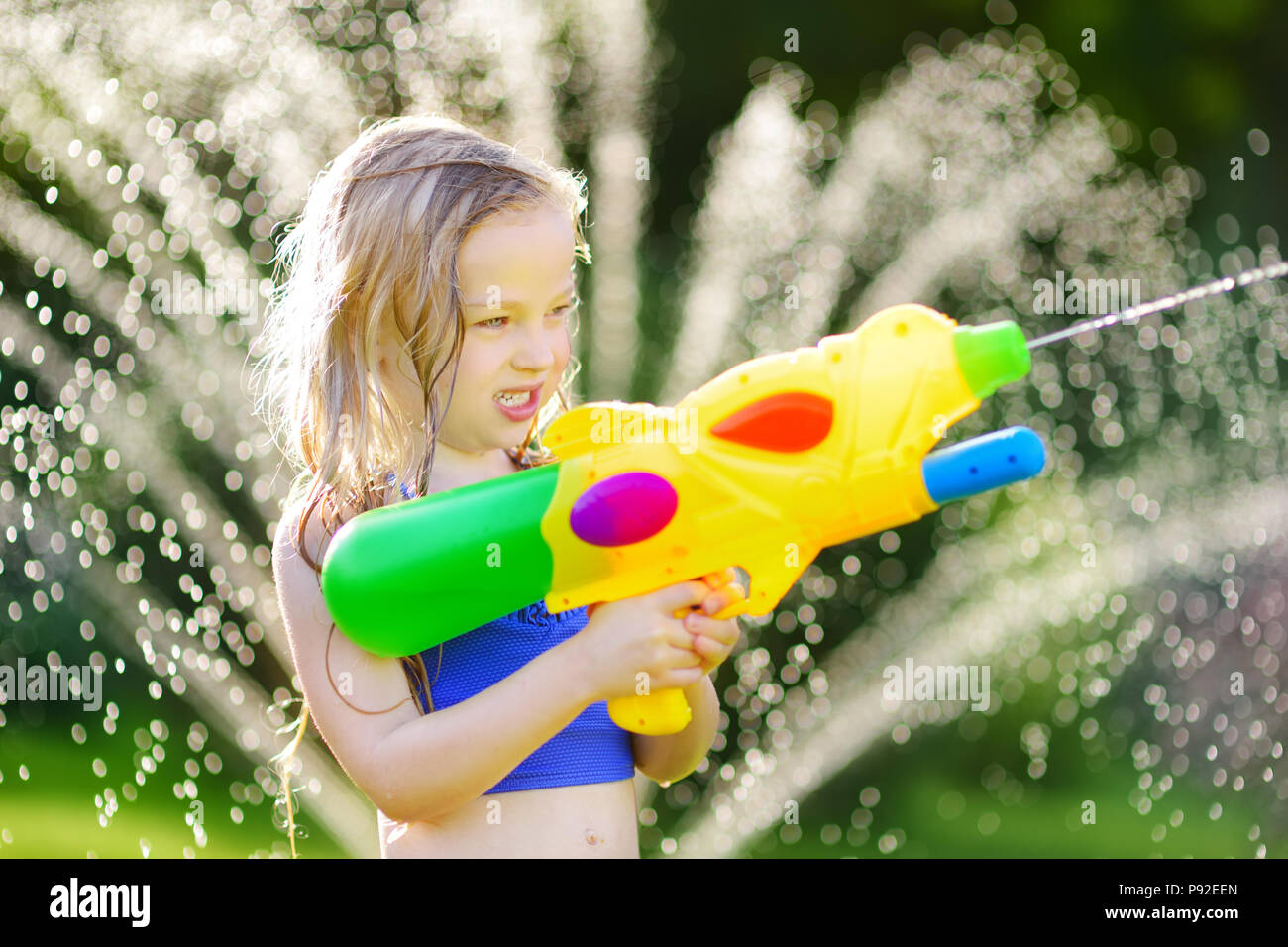 Adorable little girl playing with water gun on hot summer day. Cute