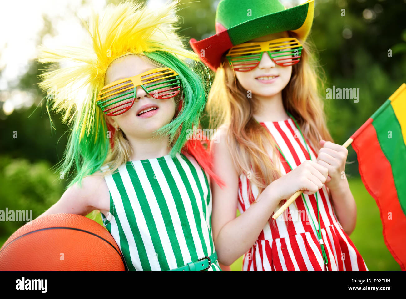 Two funny little sisters supporting and cheering their national basketball team during basketball championship. Two cute Lithuanian team fans. Stock Photo
