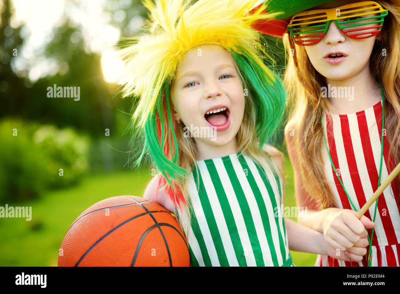 Two funny little sisters supporting and cheering their national basketball team during basketball championship. Two cute Lithuanian team fans. Stock Photo