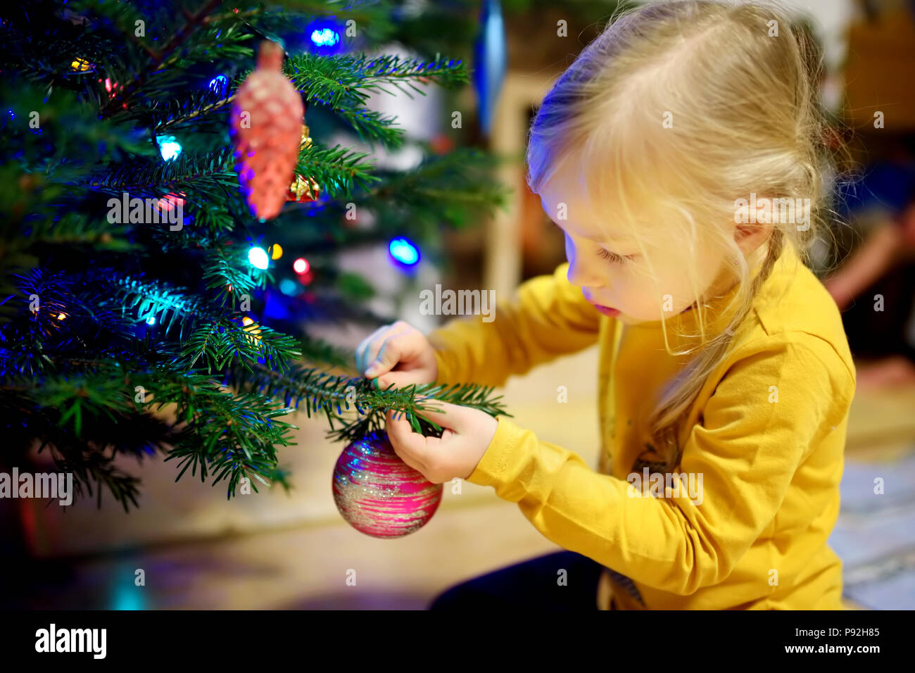 Adorable little girl decorating the Christmas tree with colorful glass
