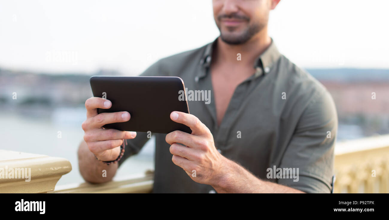 Young casual caucasian man using tablet outdoors in city, depth of field, selective focus Stock Photo