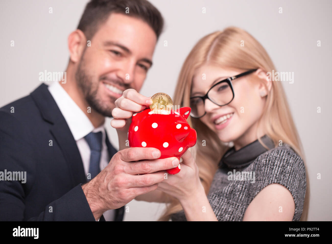 Happy young couple drop bitcoin into piggy bank, depth of field Stock Photo