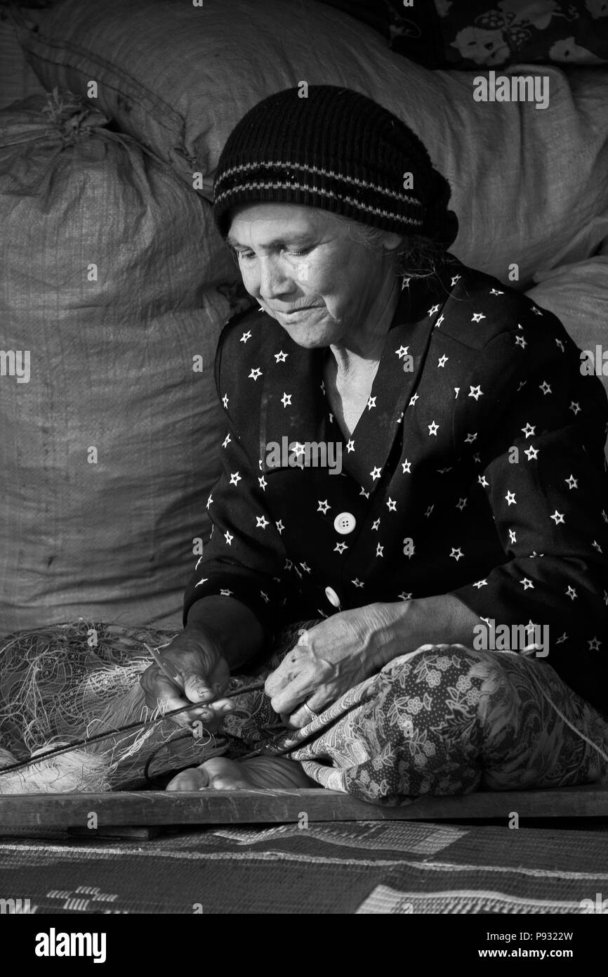A fishermans' wife repairs a fishing net in the village of Tung Nang Dam located on the North Andaman Sea - THAILAND	 Stock Photo