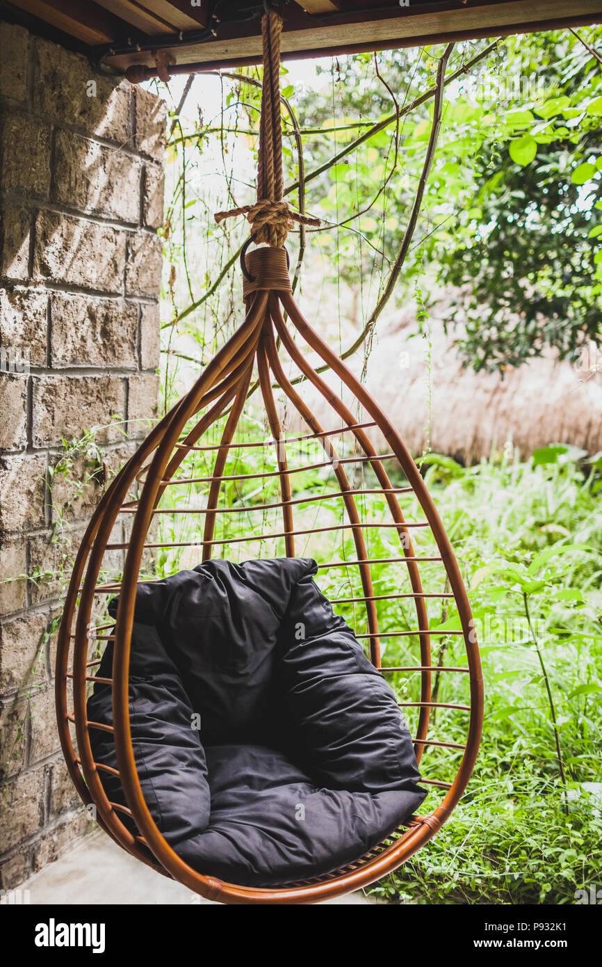 Rattan hanging wicker chair with black pillow in garden, summertime Stock Photo