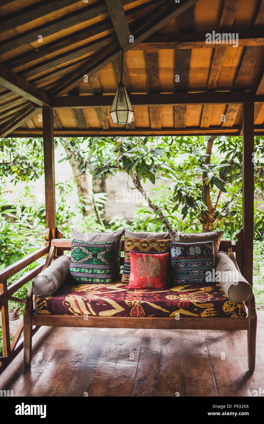 Wooden sofa with pillows on terrace under roof in ethnic style with colorful traditional ornaments Stock Photo