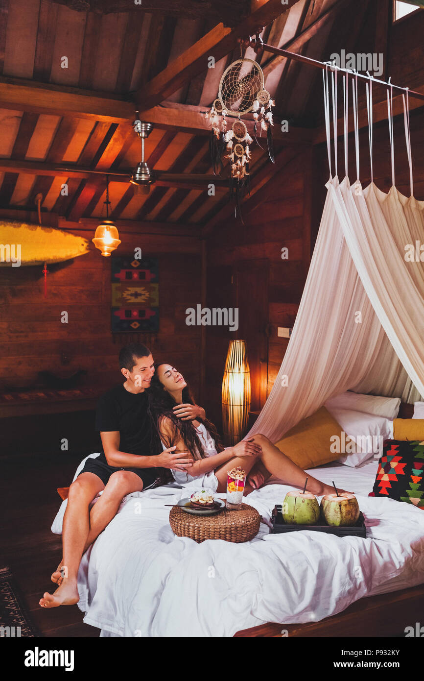 Young couple in love having breakfast in bed in traditional indian wooden house in hippie style Stock Photo