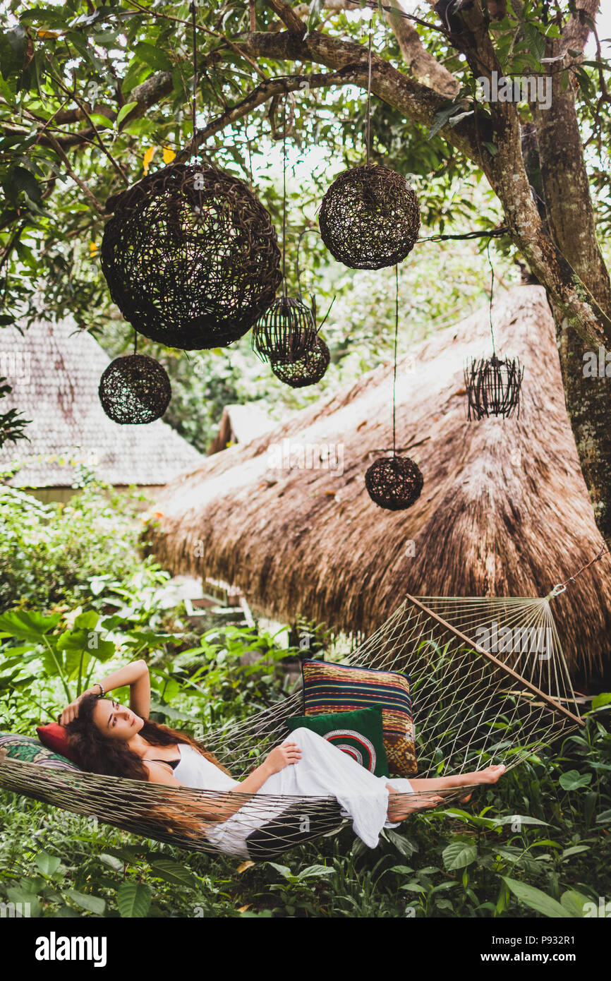 Woman in white dress relaxing in hanging hammock in bali garden. Round wooden wicker lantern hanging on tree Stock Photo Alamy