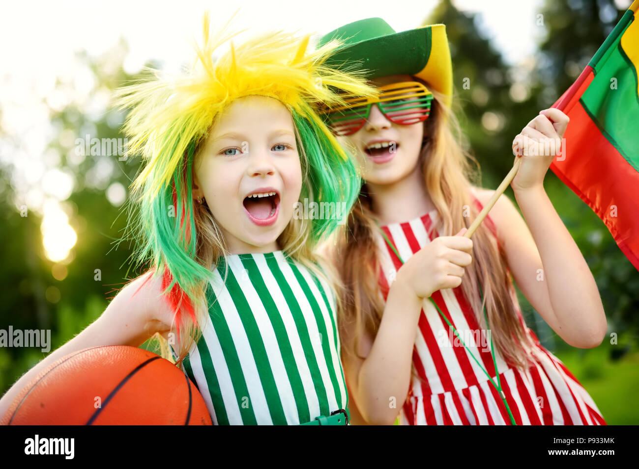 Two funny little sisters supporting and cheering their national basketball team during basketball championship. Two cute Lithuanian team fans. Stock Photo