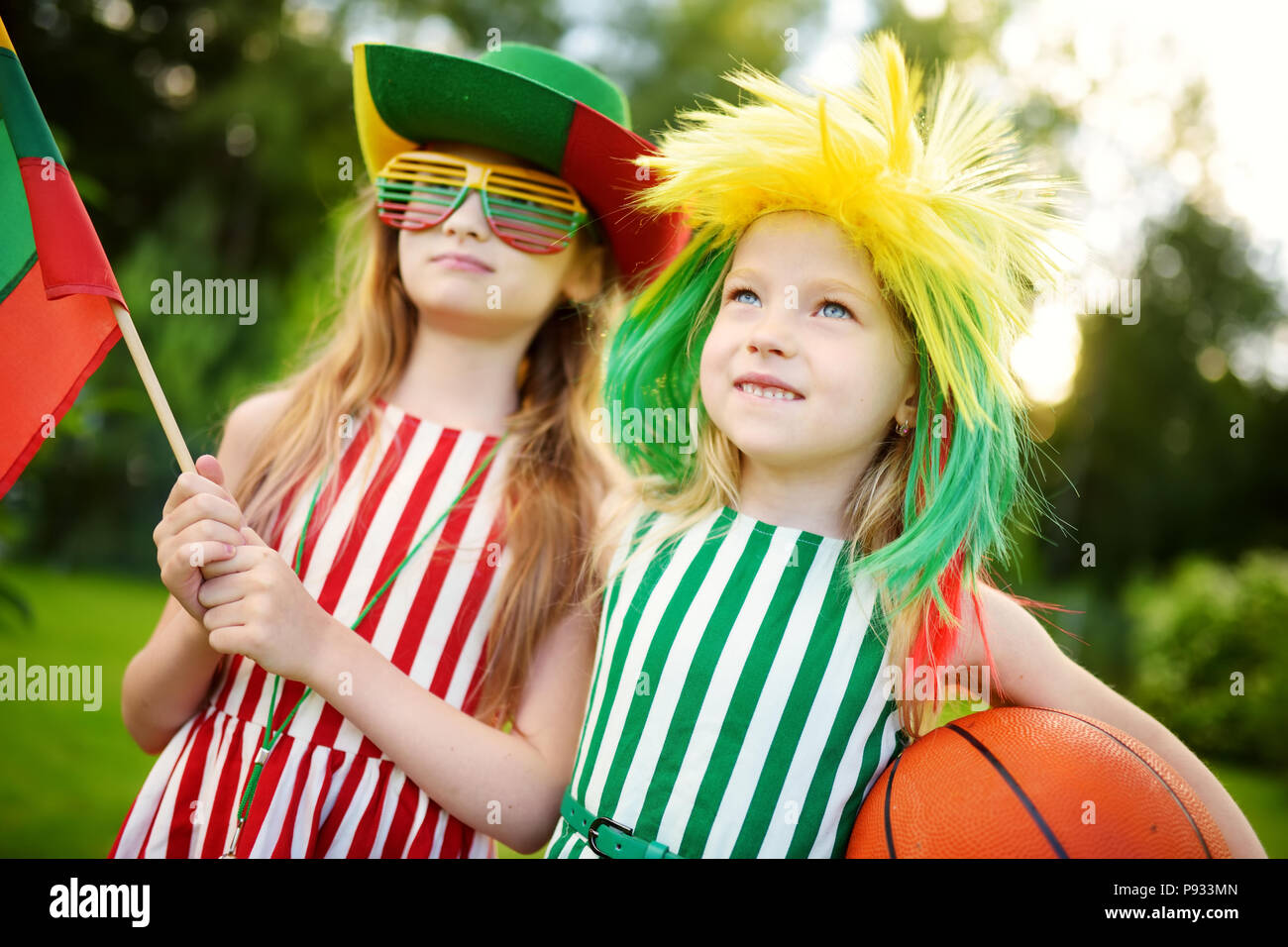 Two funny little sisters supporting and cheering their national basketball team during basketball championship. Two cute Lithuanian team fans. Stock Photo