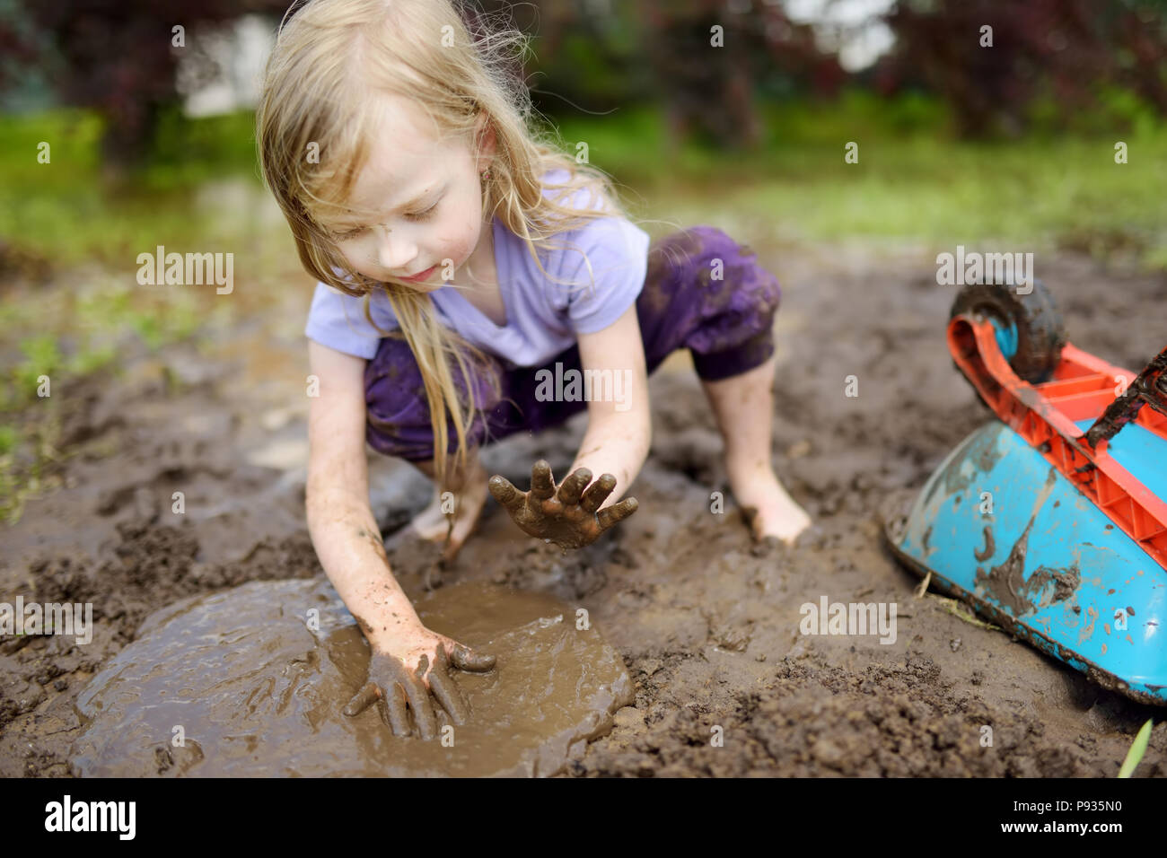 Funny little girl playing in a large wet mud puddle on sunny summer day