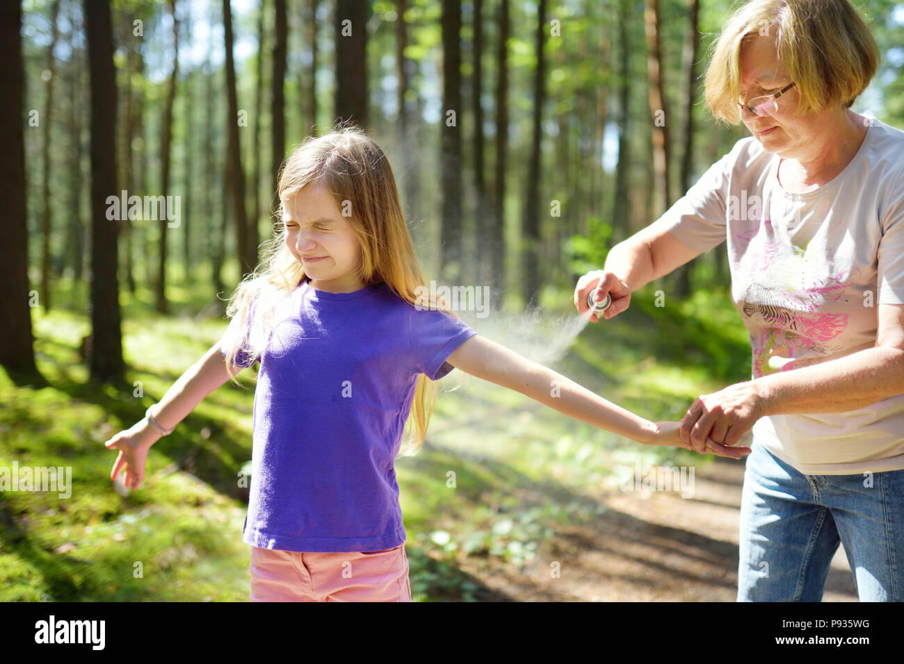 Middle age woman applying insect repellent to her granddaughter before forest hike beautiful summer day. Protecting children from biting insects at su Stock Photo