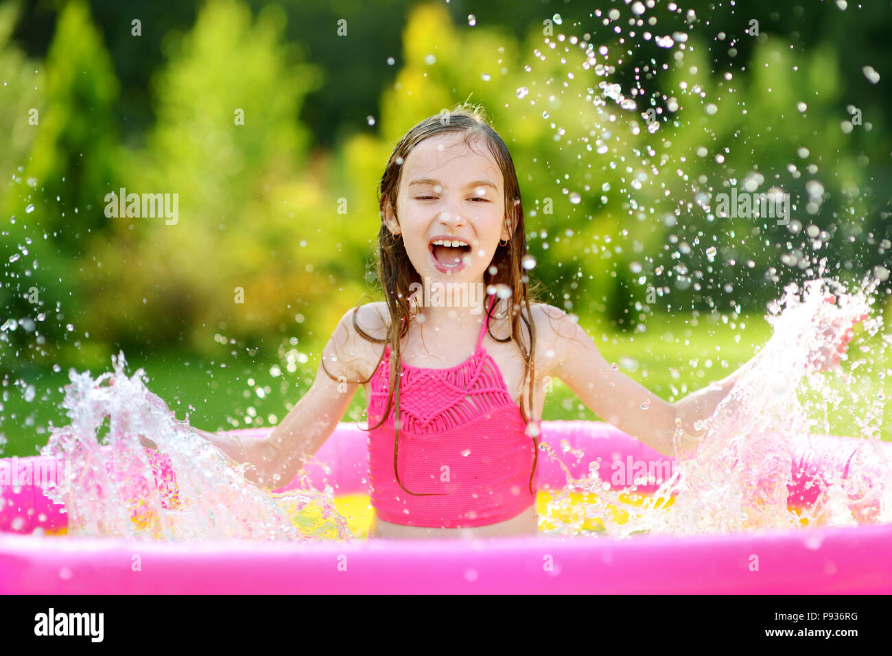 Adorable little girl playing in inflatable baby pool. Happy kid