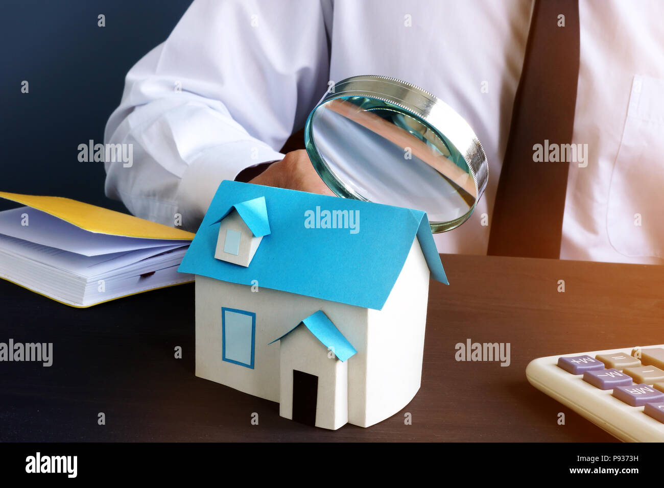 Real estate assessment. Man looking through magnifying glass on model of house. Stock Photo