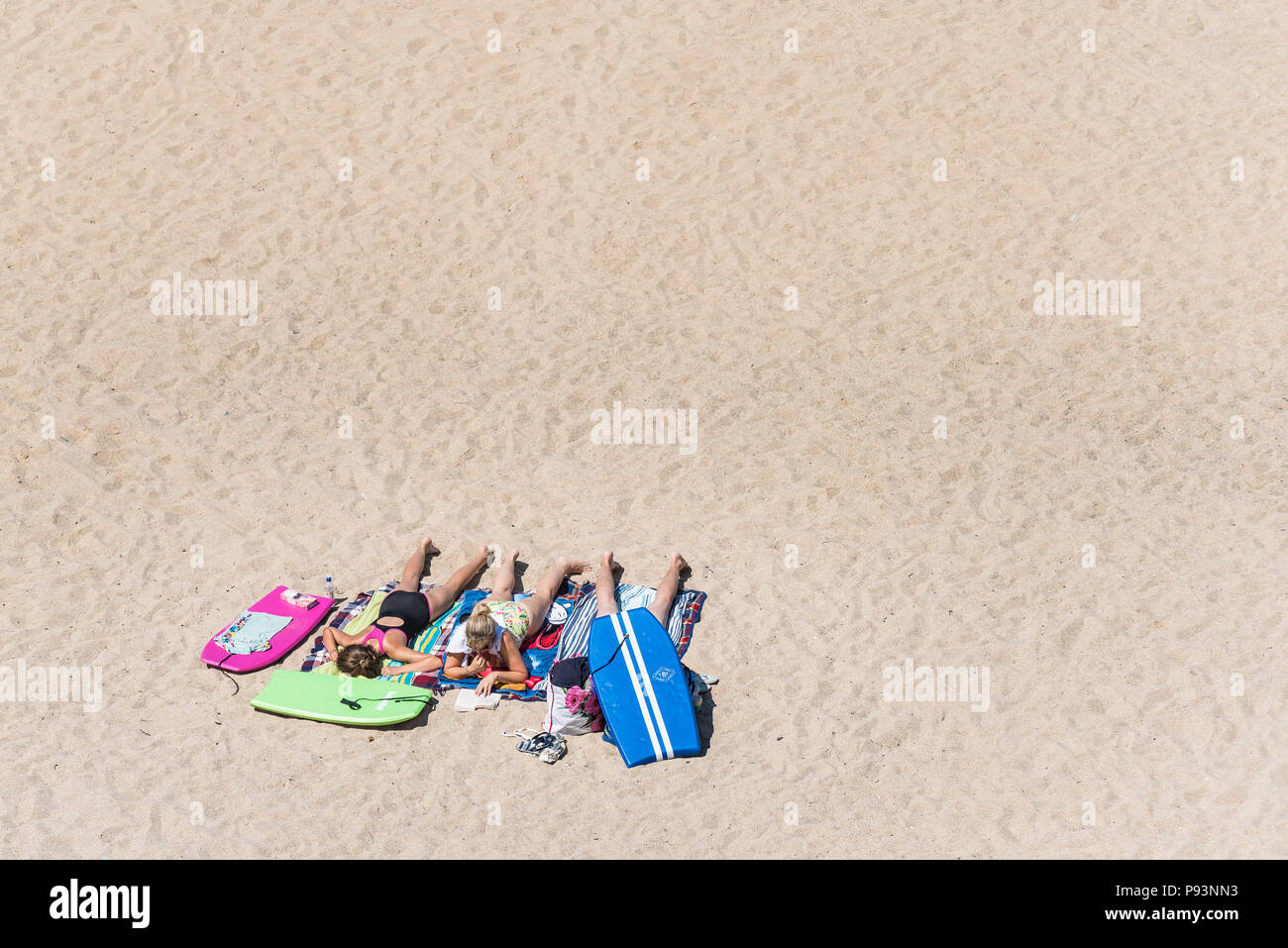 Female holidaymakers on a staycation holiday sunbathing on a sandy beach in Newquay in Cornwall. Stock Photo