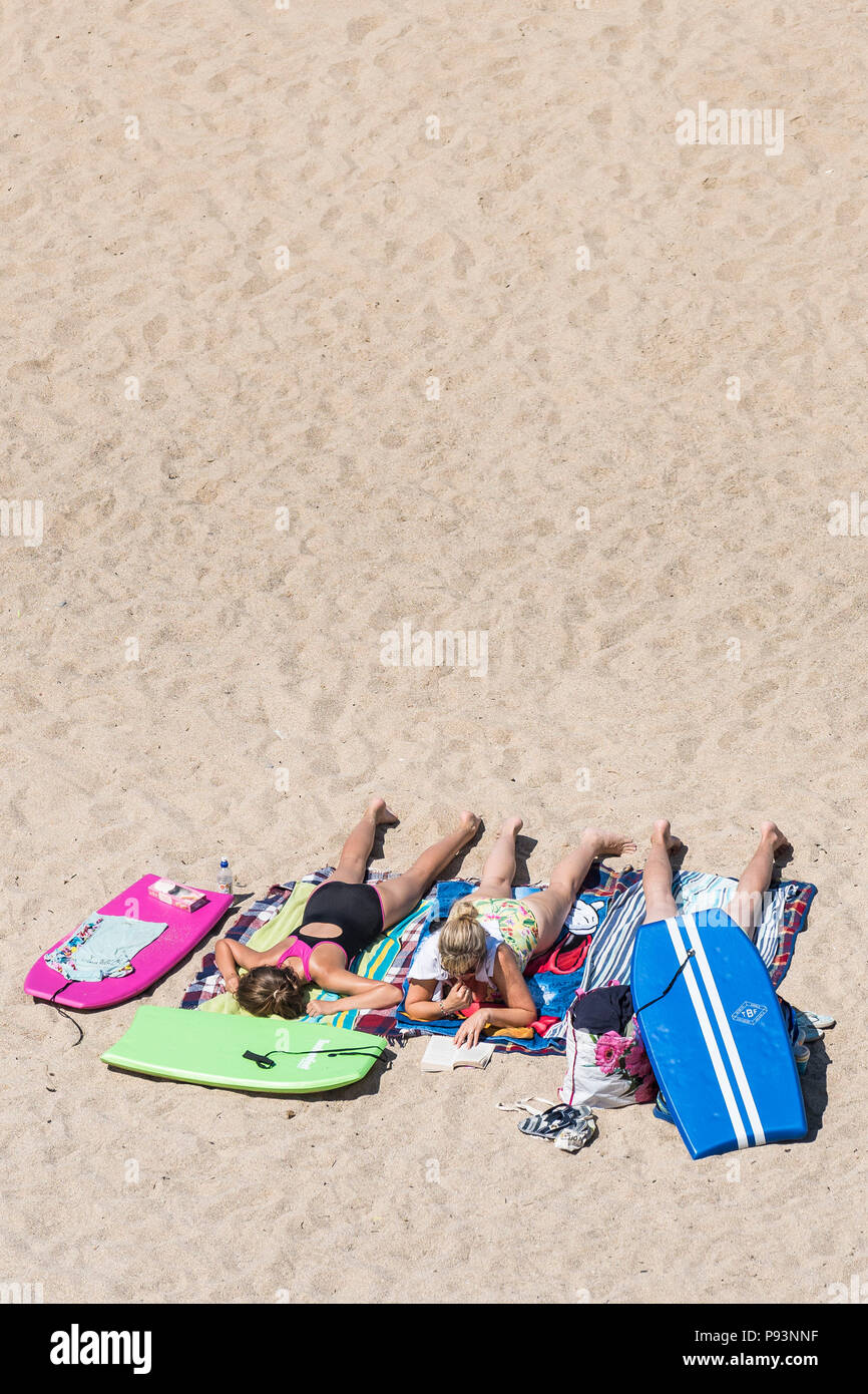 Female holidaymakers sunbathing on a sandy beach in Newquay in Cornwall. Stock Photo
