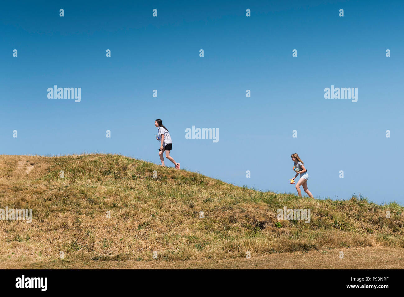 Young teenage girls walking up the remains of a Bronze Age barrow or tumulus in Newquay in Cornwall. Stock Photo
