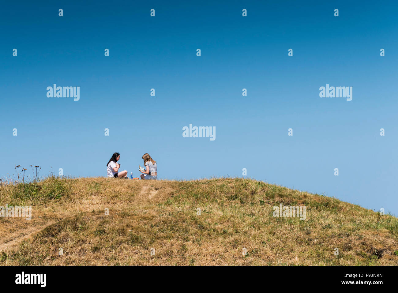 Young teenage girls sitting and chatting on the top of the remains of a Bronze Age barrow or tumulus in Newquay in Cornwall. Stock Photo