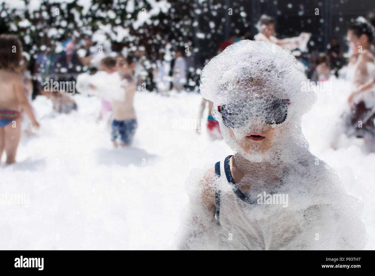 FOAM PARTY ON THE BEACH. FUNNY CHILD HAVING FUN AND COVERED IN SOAP