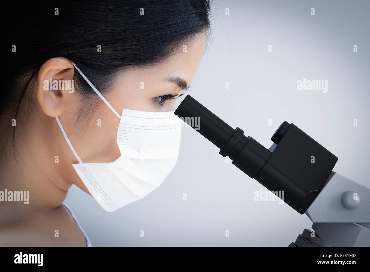 Asian scientist wearing face mask and looking at microscope Stock Photo