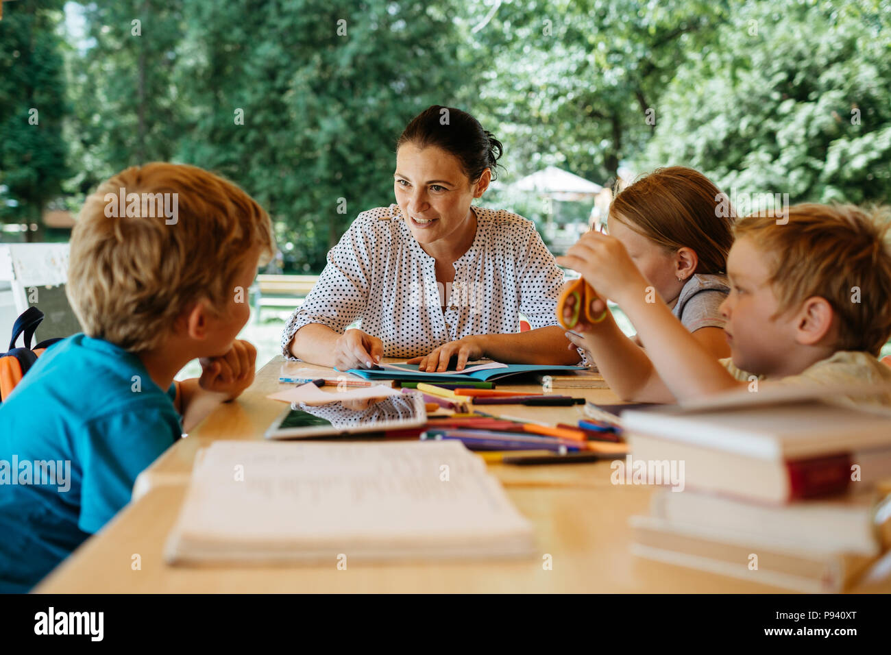 Kids during a reading lesson outside in a park. Teacher reading to children during a school break. Stock Photo