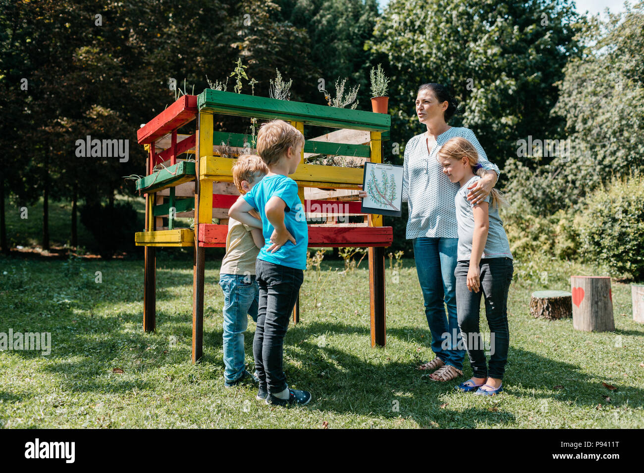 Teacher explaining an environmental topic about herbs to a small group of primary students. Outdoor learning - children discussing with a teacher. Stock Photo