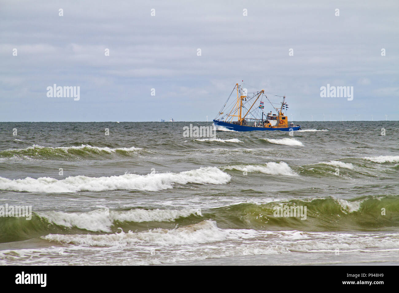 Blue fishing cutter sailing close to the coast, breakers in the foreground Stock Photo