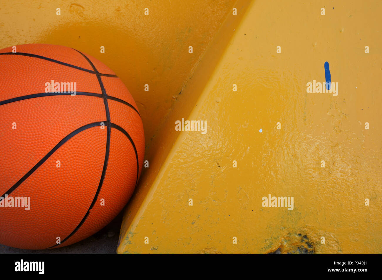 Orange basketball lying under yellow wall. Free copy space Stock Photo