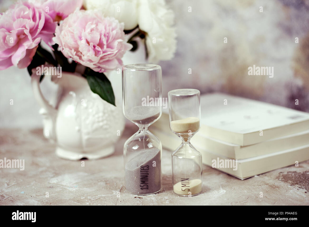 Time passing concept,urgency and running out of time. Sand fall in hourglass on working desk with books and flowers Stock Photo