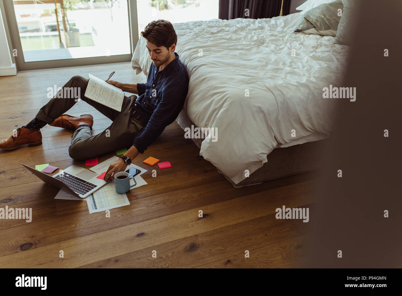businessman working on laptop computer sitting at home with his diary and official papers. Man making notes in diary and looking at laptop sitting on Stock Photo