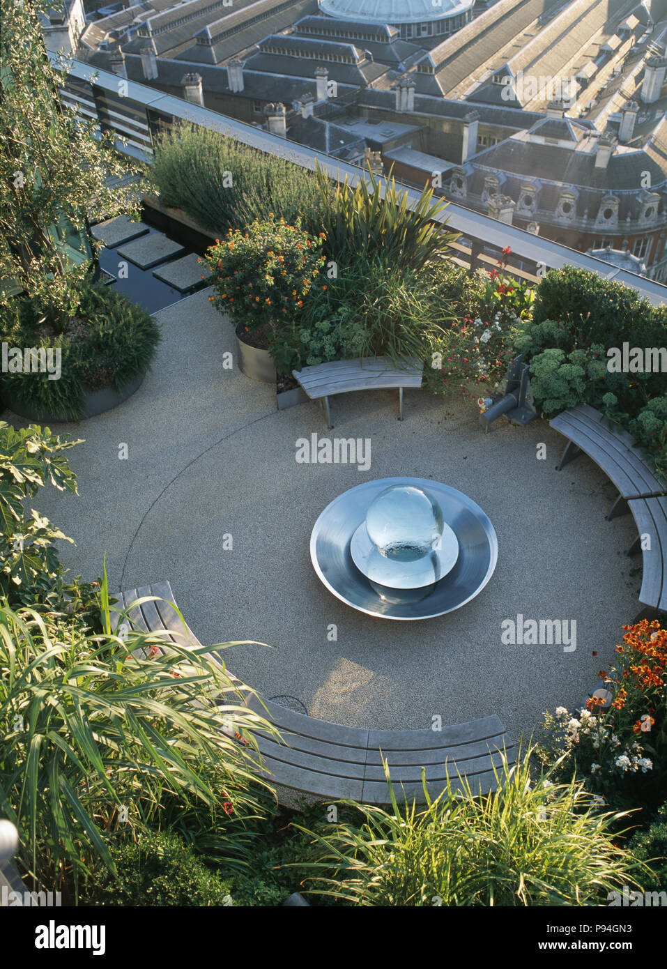 Birdseye view of curved benches around chrome bubble pool on lushly planted city roof terrace Stock Photo